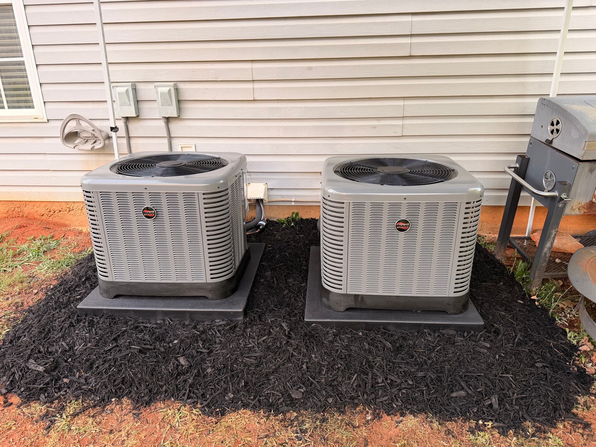 Two Ruud outdoor condensers installed beside a home